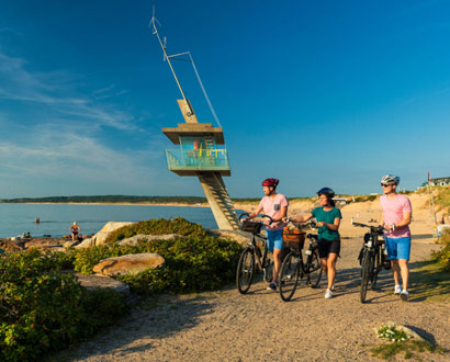 Tre personer leder sina cyklar i Tylösand vid havet vid livräddartornet i Halmstad