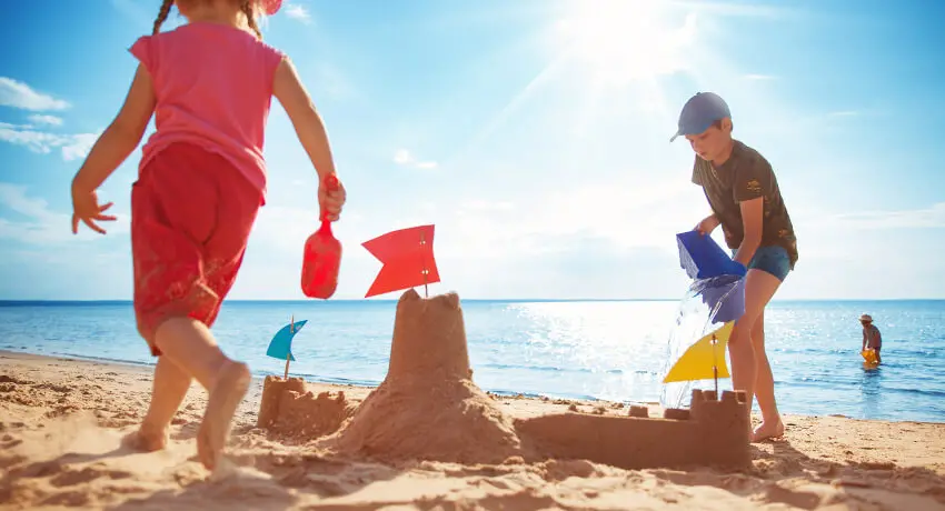 Barn bygger sandslott och leker vid strandkanten
