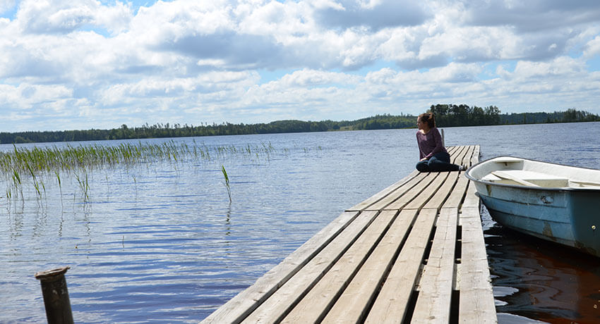 A person sits on a pier by a lake