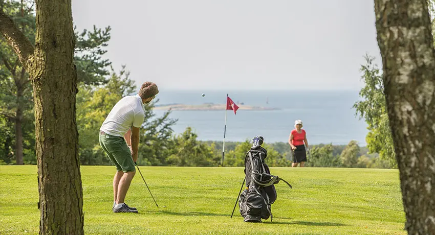 Person spelar golf med vy över havet