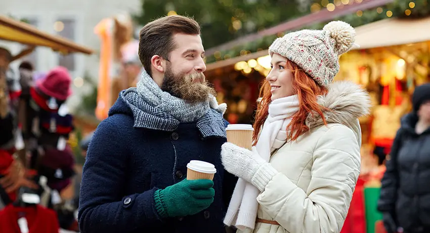 Två personer dricker en varm dryck på julmarknad